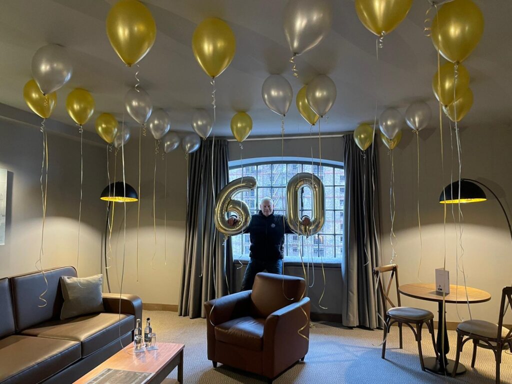 Gold and silver ceiling balloons with a jumbo 6 and 0 for a 60th birthday party in a hotel room